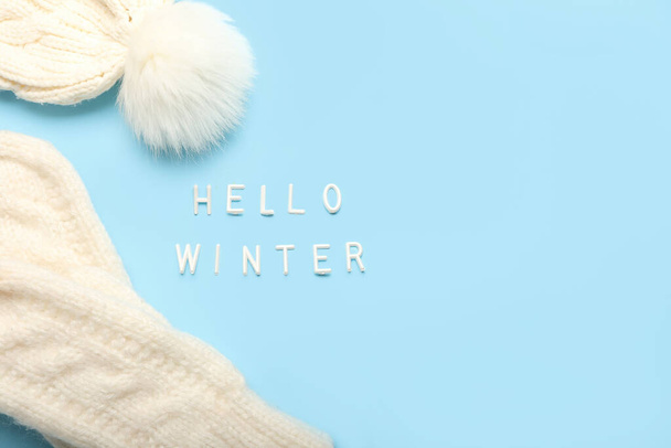 Text HELLO WINTER, knitted mittens and hat on color background, closeup - Photo, Image