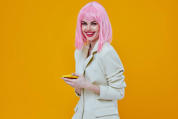 Nainen puhelin käsissään vaaleanpunainen tukka studio keltainen tausta - Valokuva, kuva