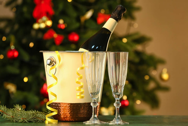 Bucket with bottle of champagne and glasses on table against blurred background - Photo, Image