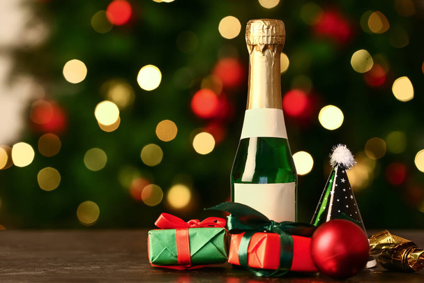 Bottle of champagne with gift boxes and Christmas decor on table against blurred background - Photo, image