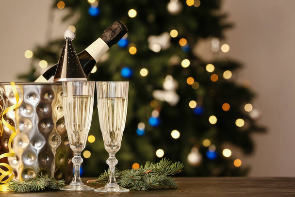 Ведро с бутылкой шампанского, шляпой для вечеринок и бокалами на столе на размытом фоне - Фото, изображение