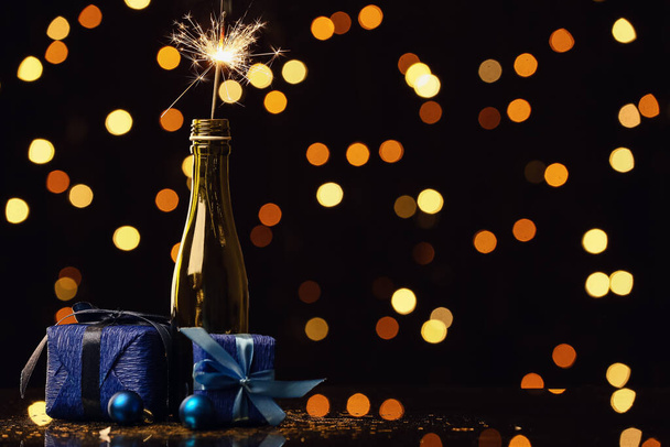 Egy üveg pezsgő karácsonyi csillagszóróval és ajándékdobozokkal az asztalon homályos háttérrel - Fotó, kép