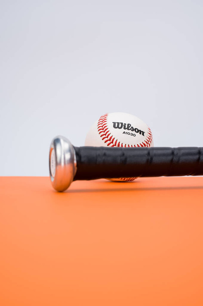 INVERIGO, ITALY - Dec 08, 2021: isolated baseball ball and bat on an orange background with text space - Zdjęcie, obraz