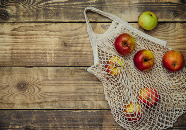 Zero waste concept, reusable mesh shopping bags.Eco-bag made of natural cotton fabric on a wooden background.Ripe apples in a shopping bag. - 写真・画像