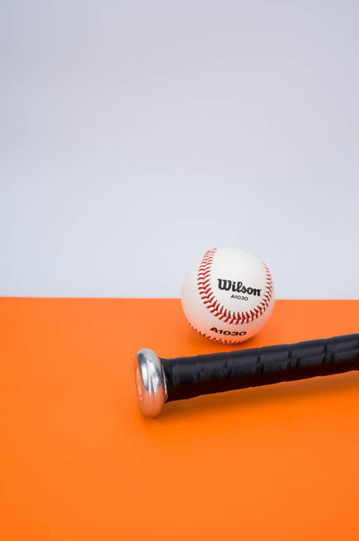 INVERIGO, ITALY - Dec 08, 2021: isolated baseball ball and bat on an orange background with text space - Fotó, kép