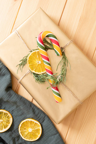 Christmas wrapped gift in eco style. Golden gift box with Christmas tree, dry orange slice and traditional candy cane. Top view. Festive mood, gift wrapping idea concept. DIY - Zdjęcie, obraz