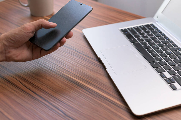 Zbliżenie człowieka za pomocą smartfona przy biurku z laptopem - Zdjęcie, obraz