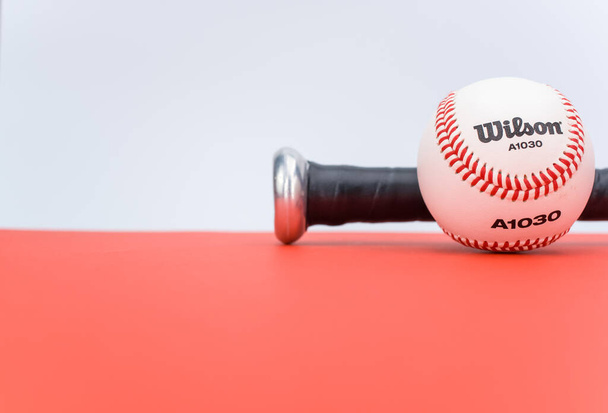 INVERIGO, ITALY - Dec 08, 2021: isolated baseball ball and bat on a red background with text space - Foto, Bild