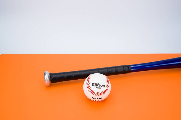 INVERIGO, ITALY - Dec 08, 2021: isolated baseball ball and bat on an orange background with text space - Fotografie, Obrázek