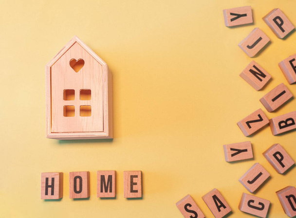 The word home, taken from a stack of wooden letter blocks and a wooden house in the yellow background with a copy space - Фото, изображение