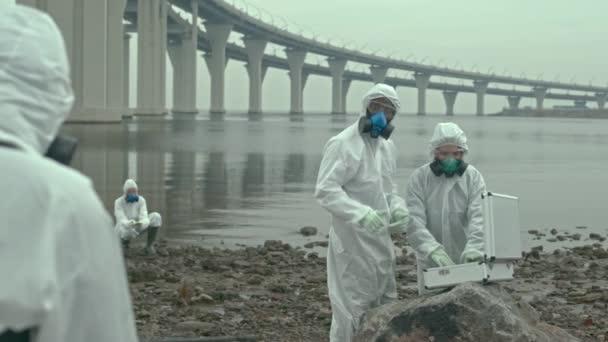 バイオハザード災害後の汚染された海岸を探索しながら、油漏れの除去と水と土壌サンプルの収集方法を議論する科学者のグループのスローショット - 映像、動画
