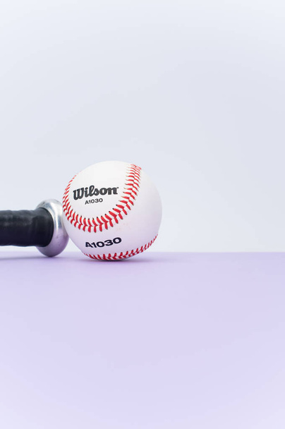 INVERIGO, ITALY - Dec 08, 2021: isolated baseball ball and bat on a lilac background with text space - 写真・画像