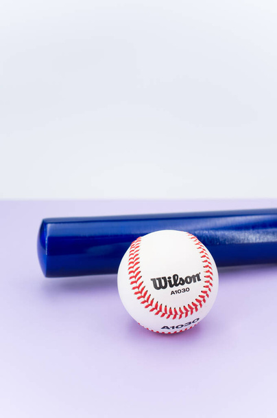 INVERIGO, ITALY - Dec 08, 2021: isolated baseball ball and bat on a lilac background with text space - Fotó, kép