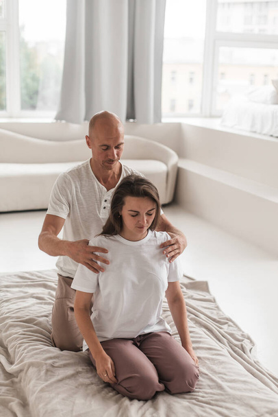 Un giovane professionista che fissa la colonna vertebrale di una donna in una stanza bianca e accogliente durante una terapia manuale - Foto, immagini