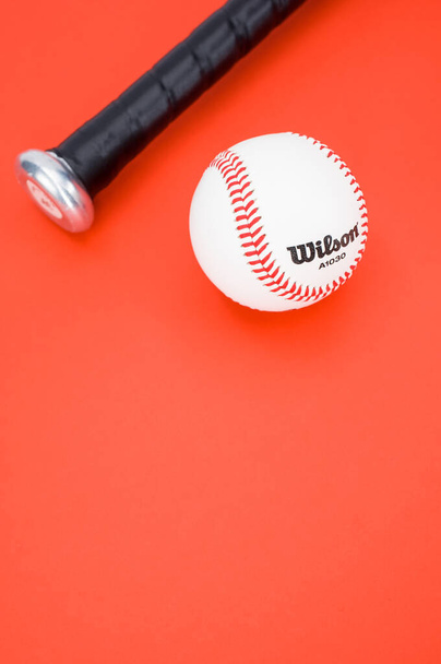 INVERIGO, ITALY - Dec 08, 2021: isolated baseball ball and bat on a red background with text space - Zdjęcie, obraz