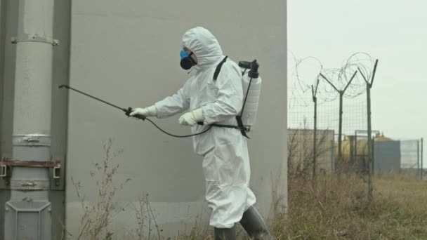 Медленный снимок мужчины-эколога в защитном покрытии дезинфицирующее средство с распылителем на поверхности объектов, стоящих на загрязненной территории, где произошла биологическая катастрофа - Кадры, видео