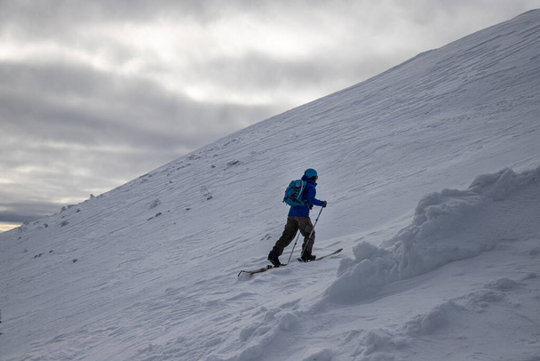 An adult tourist skiing on pistes on a mountain in a resort area under a cloudy sky - Foto, Bild