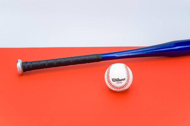 INVERIGO, ITALY - Dec 08, 2021: isolated baseball ball and bat on a red background with text space - Foto, afbeelding