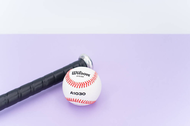 INVERIGO, ITALY - Dec 08, 2021: isolated baseball ball and bat on a lilac background with text space - Φωτογραφία, εικόνα