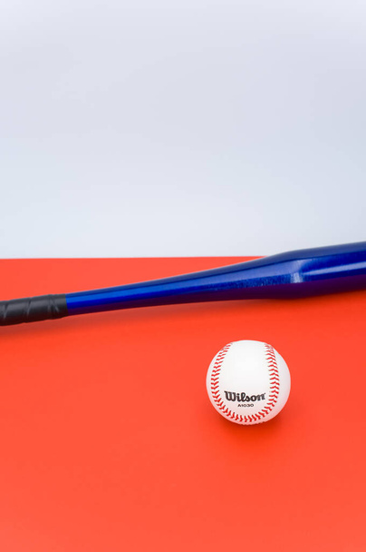 INVERIGO, ITALY - Dec 08, 2021: isolated baseball ball and bat on a red background with text space - Foto, afbeelding