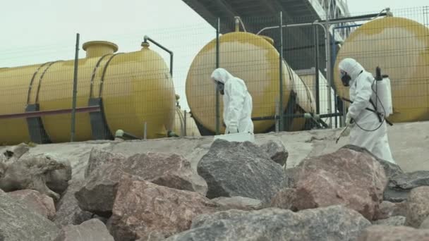 Медленный снимок двух экспертов-экологов-мужчин в защитном комбинезоне, несущих рабочее оборудование, идущее по загрязненной территории, где произошла экологическая катастрофа - Кадры, видео