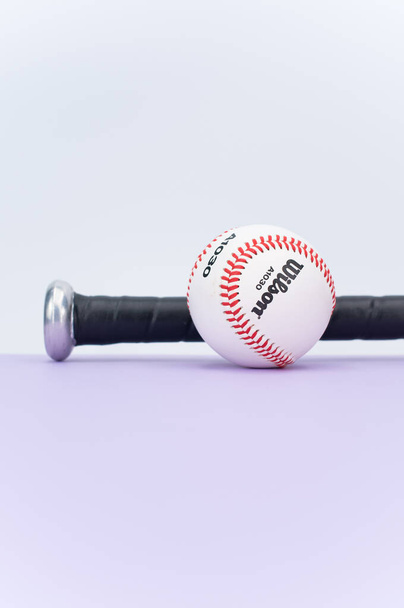 INVERIGO, ITALY - Dec 08, 2021: isolated baseball ball and bat on a lilac background with text space - Φωτογραφία, εικόνα