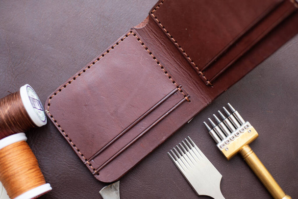 Billetera marrón de cuero genuino para hombre sobre fondo de cuero con herramienta artesanal - Foto, Imagen