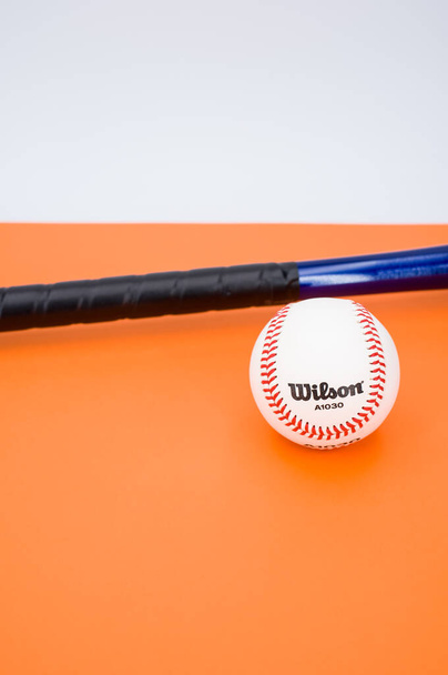 INVERIGO, ITALY - Dec 08, 2021: isolated baseball ball and bat on an orange background with text space - Foto, afbeelding