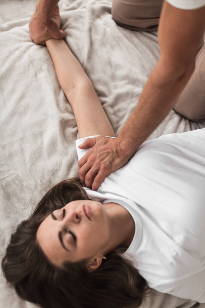 A professional young man massaging a woman's arms in a white cozy room during a manual therapy - Foto, afbeelding