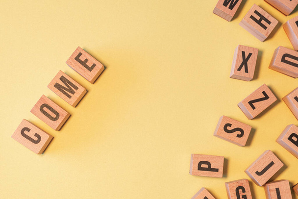 The word COME, taken from a pile of wooden letter blocks with yellow background and copy space - Foto, Imagem