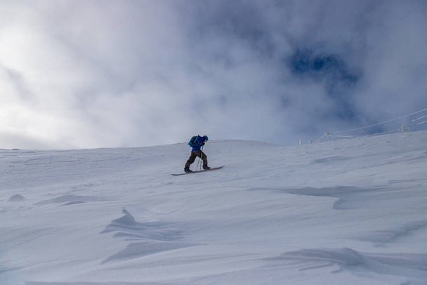 An adult tourist skiing on pistes on a mountain in a resort area under a cloudy sky - Foto, Imagen