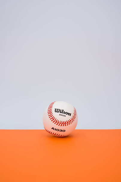 INVERIGO, ITALY - Dec 08, 2021: isolated baseball ball on orange paper background with text space - Fotografie, Obrázek