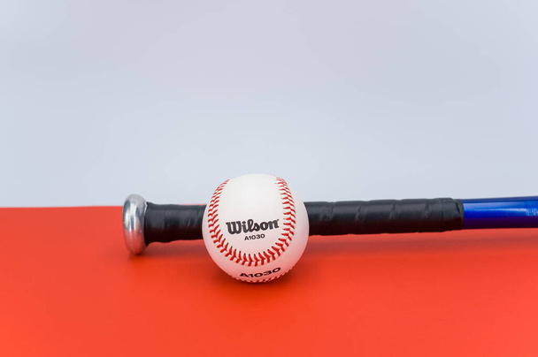 INVERIGO, ITALY - Dec 08, 2021: isolated baseball ball and bat on a red background with text space - Φωτογραφία, εικόνα