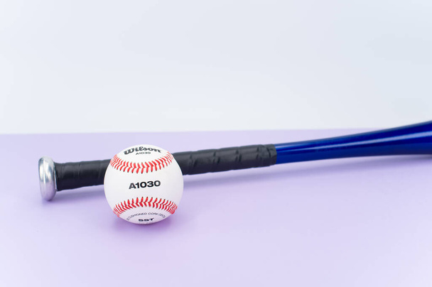 INVERIGO, ITALY - Dec 08, 2021: isolated baseball ball and bat on a lilac background with text space - Fotografie, Obrázek