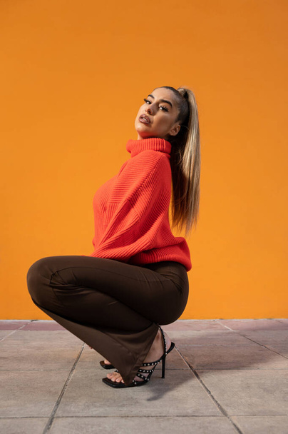 A squatting sexy Spanish girl posing in the orange background - Foto, Imagen