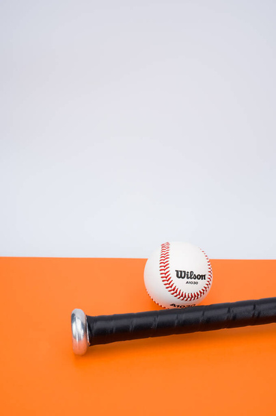 INVERIGO, ITALY - Dec 08, 2021: isolated baseball ball and bat on an orange background with text space - Fotografie, Obrázek