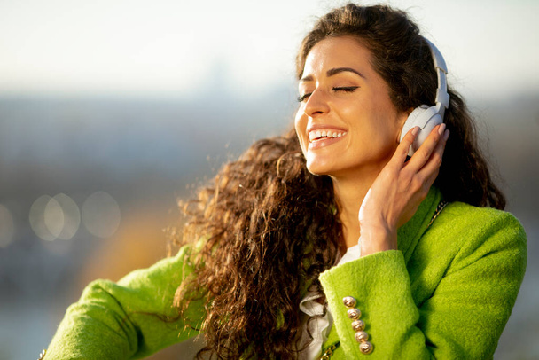 美しい若い巻き毛の女性は、晴れた秋の日に川でスマートフォンで音楽を聞いています - 写真・画像
