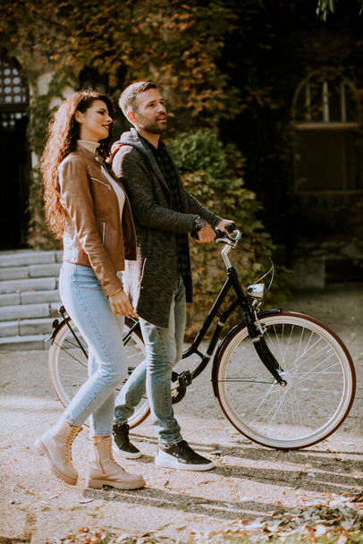 Komea nuori pari kävelee polkupyörällä syksyllä puistossa - Valokuva, kuva