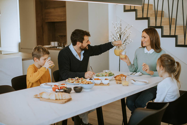 Genç mutlu aile, evdeki yemek masasında kahvaltı ederken konuşuyor. - Fotoğraf, Görsel