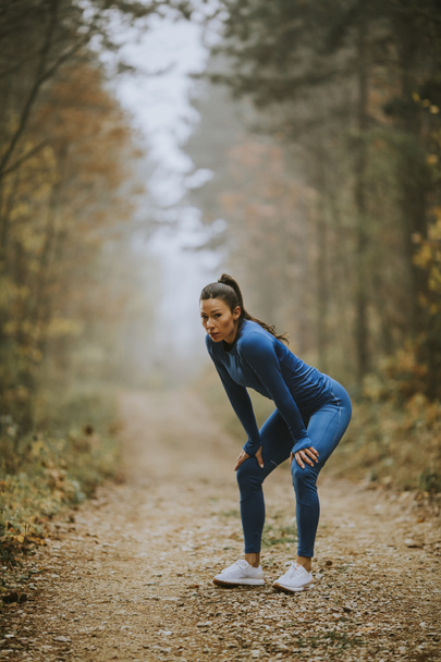 Bella giovane donna fare una pausa durante l'esercizio all'aperto sul sentiero forestale in autunno - Foto, immagini