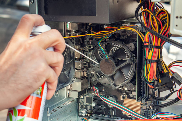 Maintenance and cleaning of the insides of the computer. Mans hand holds a cylinder of compressed air and cleans the insides of the computer - Photo, Image