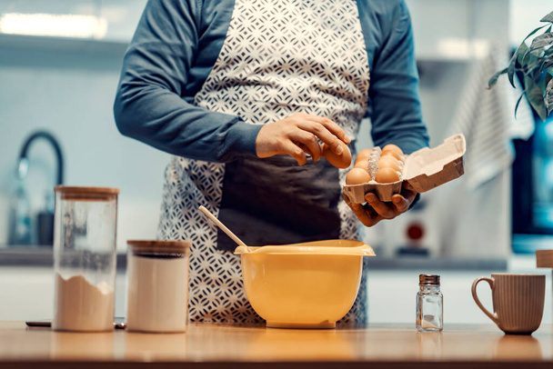Adam evde kek ya da kurabiye pişiriyor. Yumurta tutan, kırmaya ve kurabiye yapmaya hazırlanan genç bir adamın kırpılmış resmi. Yumurta tutan eller. - Fotoğraf, Görsel