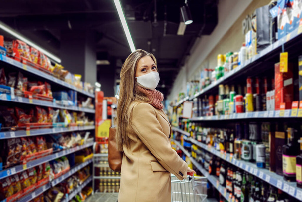 Eine Frau mit Mundschutz betritt den Laden und schiebt den Einkaufswagen. Die Frau wird Lebensmittel und Sachen für ihr Haus kaufen. Frau im Supermarkt. - Foto, Bild