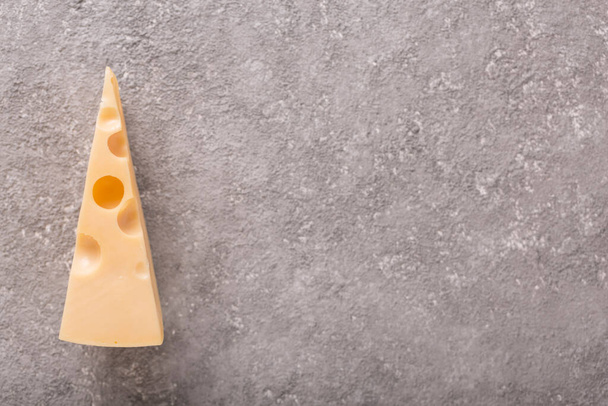 Un pezzo di formaggio Maasdam con grandi buchi su uno sfondo di cemento grigio. Primo piano - Foto, immagini