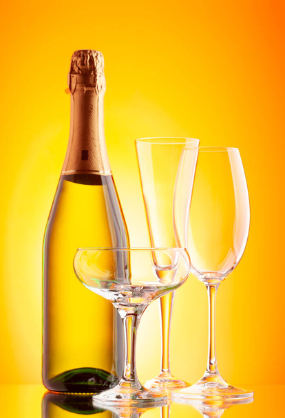 Τρία ποτήρια σαμπάνιας και μπουκάλι αφρώδους κρασιού. Πάνω από κίτρινο φόντο - Φωτογραφία, εικόνα