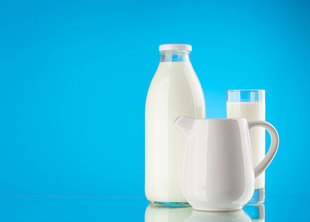 Μπουκαλάκι γάλακτος, γυάλινο και κανάτα σε μπλε φόντο με χώρο αντιγραφής. Γαλακτοκομικά - Φωτογραφία, εικόνα
