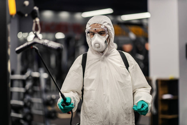 Close-up shot of a worried male person in a protective suit with goggles and mask. He committed to winning coronavirus in gym place. COVID19 prevention, pandemic situation, social distance, new normal - Photo, image