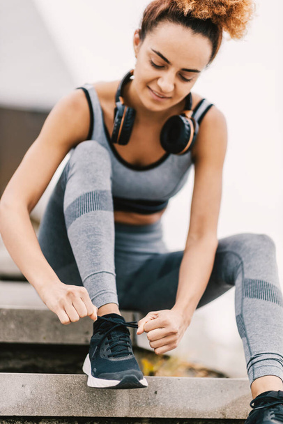 Tiefansicht einer sportlichen Frau, die auf der Treppe der Stadtstraße sitzt und einen Schnürsenkel bindet. Eine Sportlerin bereitet sich auf das Laufen vor - Foto, Bild