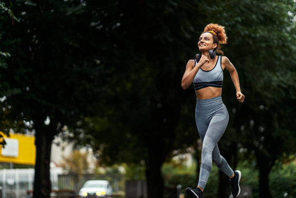 A fit female jogger is jogging on the city street. Sport regenerates body and soul. An urban runner with healthy habits. - Photo, Image