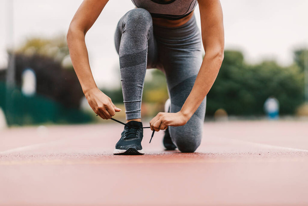 Großaufnahme einer fitten Läuferin, die auf der Bahn im Stadion kniet und Schnürsenkel an ihren Turnschuh bindet. Sie bereitet sich auf das Training vor. Ein Läufer bindet Schnürsenkel. - Foto, Bild